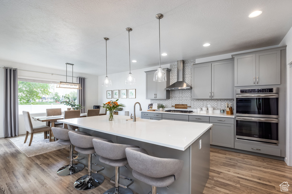 Kitchen with wall chimney range hood, gray cabinets, a breakfast bar area, backsplash, and stainless steel appliances