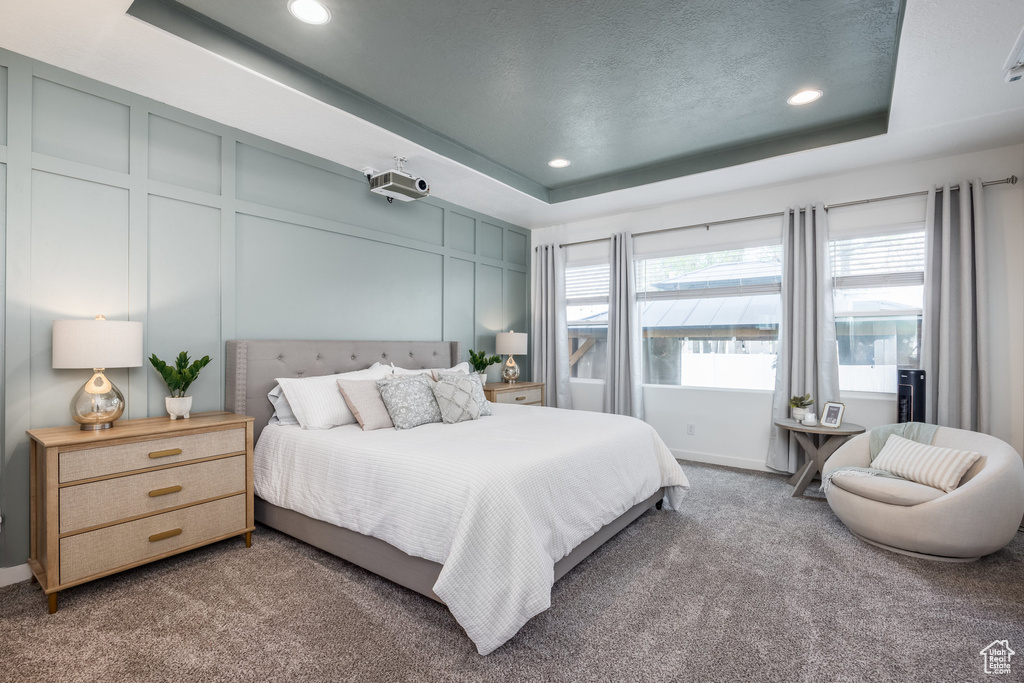 Bedroom featuring carpet floors, a decorative wall, recessed lighting, and a raised ceiling