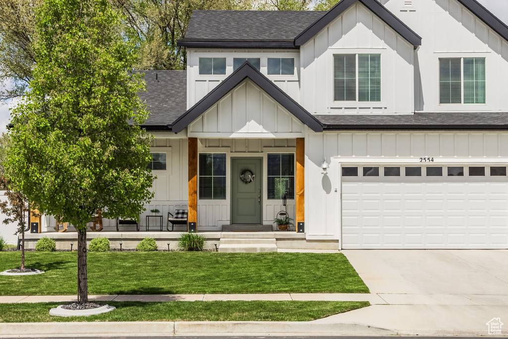 Modern farmhouse with board and batten siding, roof with shingles, a front lawn, and concrete driveway
