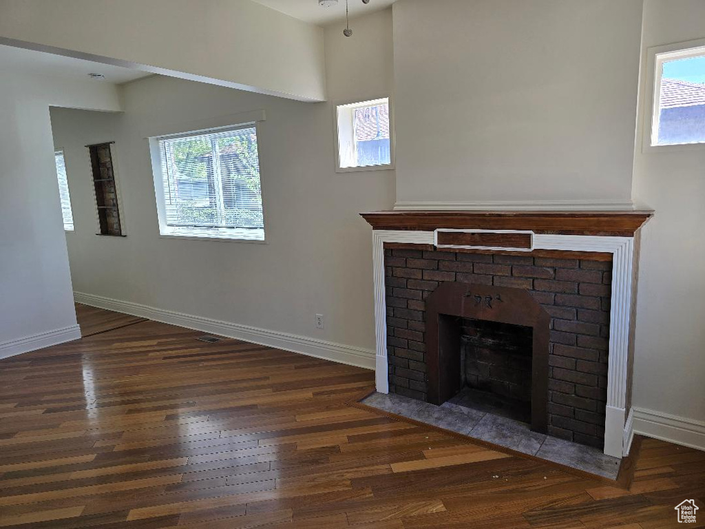 Unfurnished living room with baseboards, a fireplace, wood finished floors, and a wealth of natural light