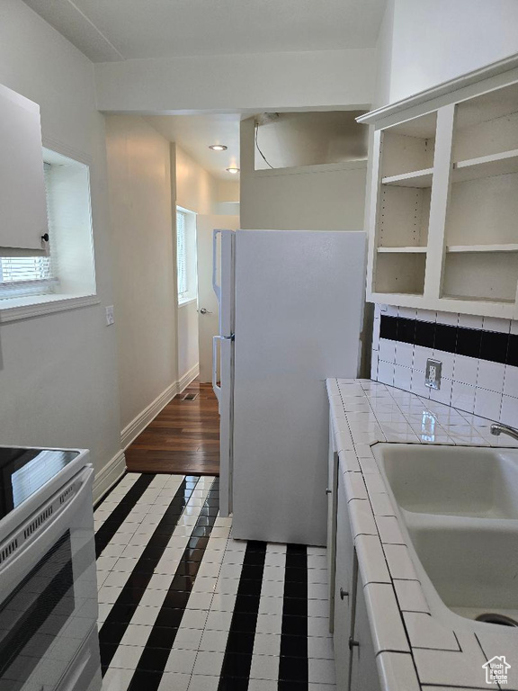 Kitchen with decorative backsplash, white appliances, baseboards, tile counters, and a sink