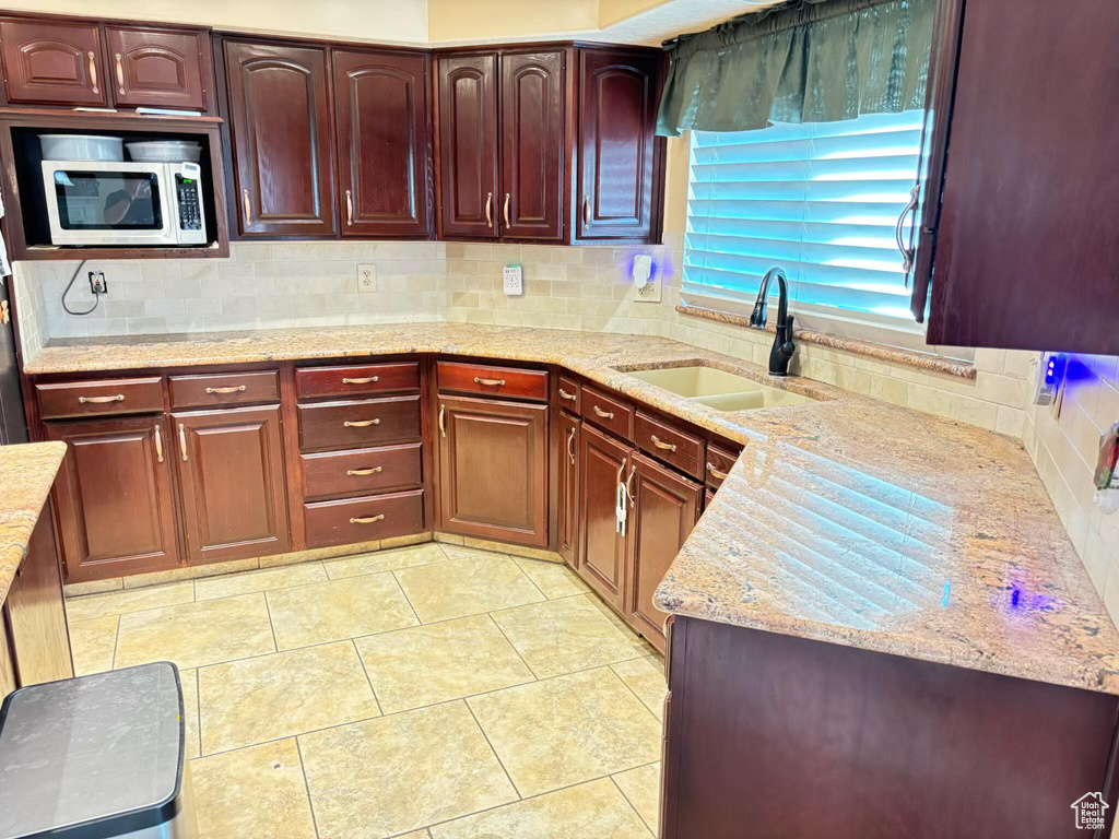 Kitchen with a sink, stainless steel microwave, tasteful backsplash, light stone countertops, and reddish brown cabinets