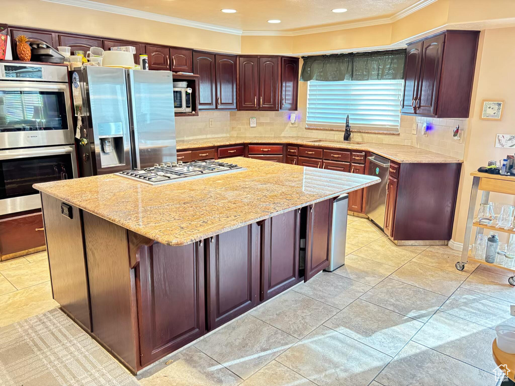 Kitchen featuring appliances with stainless steel finishes, a sink, crown molding, a center island, and light stone countertops