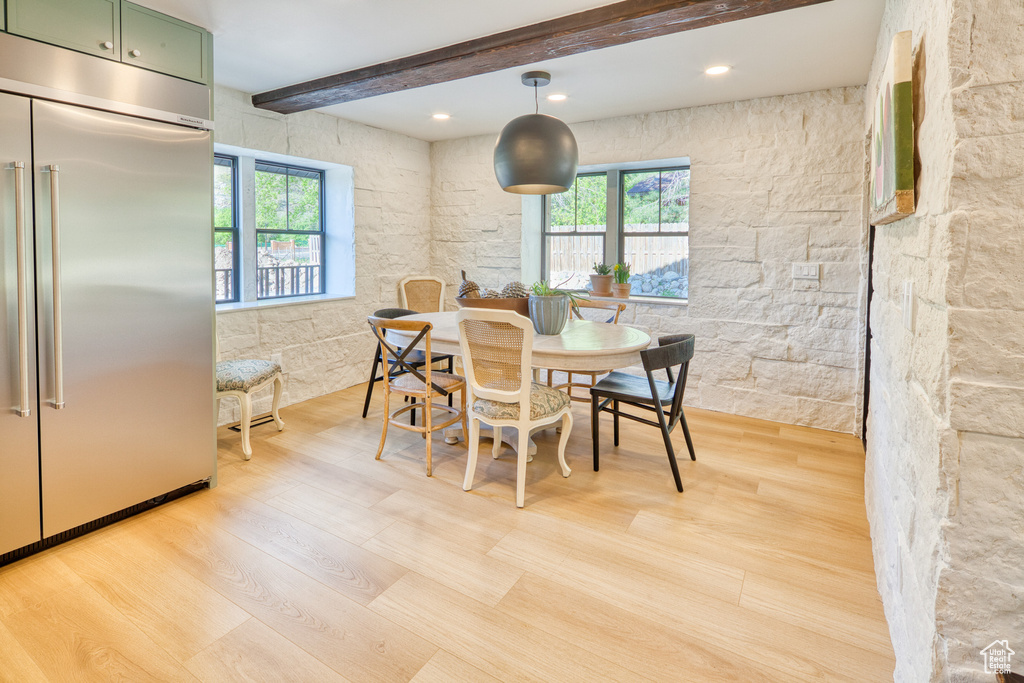 Dining room with light wood-style flooring, a healthy amount of sunlight, and beamed ceiling