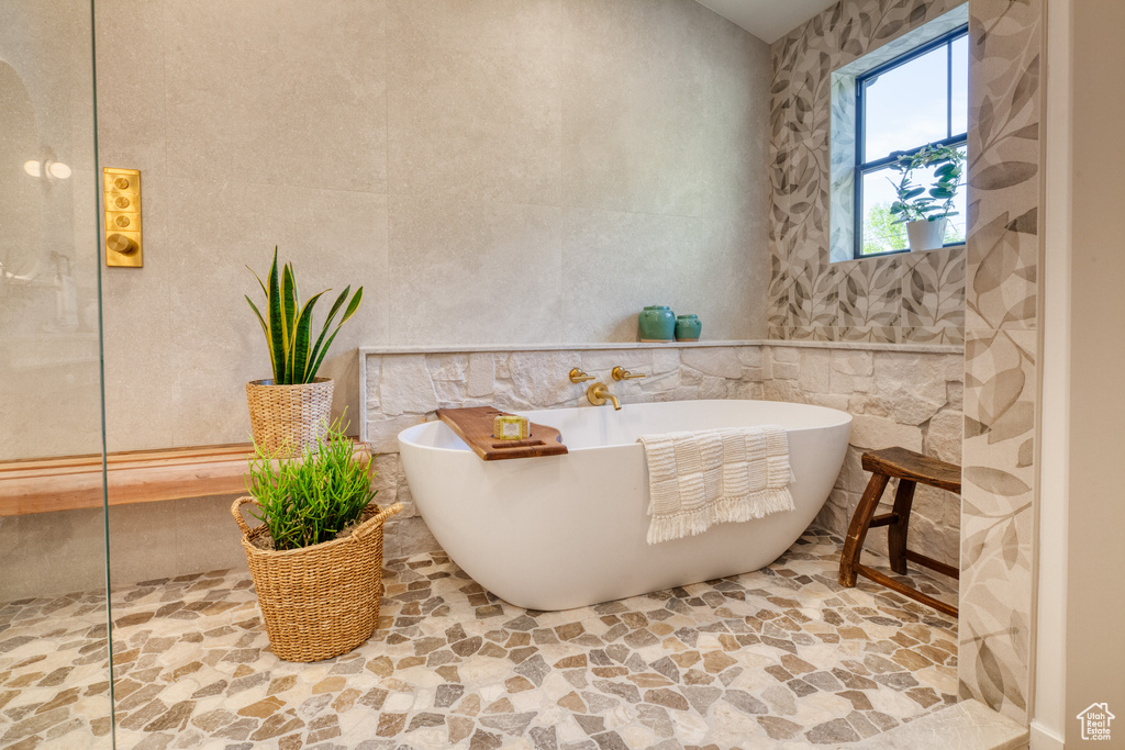 Full bath featuring stone floors, tile walls, and a freestanding tub