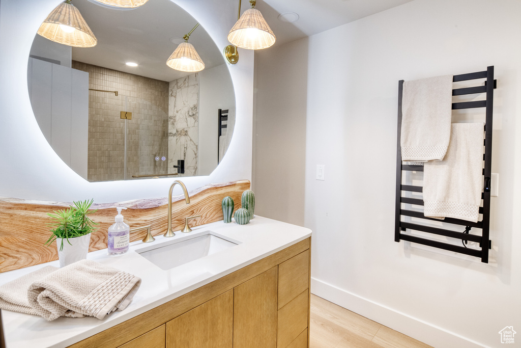 Bathroom featuring vanity, wood finished floors, baseboards, radiator heating unit, and tiled shower