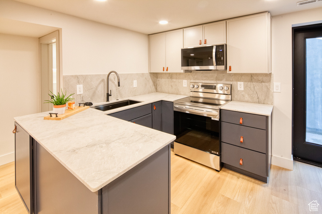 Kitchen with a sink, gray cabinets, appliances with stainless steel finishes, and light wood finished floors