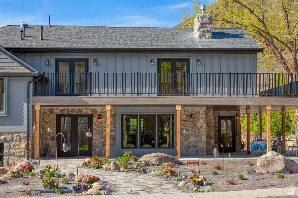 Back of property featuring stone siding, board and batten siding, a chimney, a balcony, and french doors