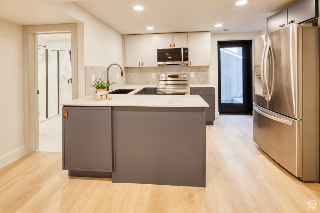 Kitchen with decorative backsplash, a peninsula, light wood-style floors, a sink, and stainless steel appliances