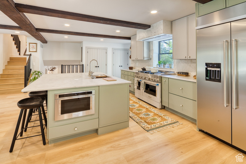 Kitchen with light countertops, high quality appliances, green cabinetry, and light wood finished floors