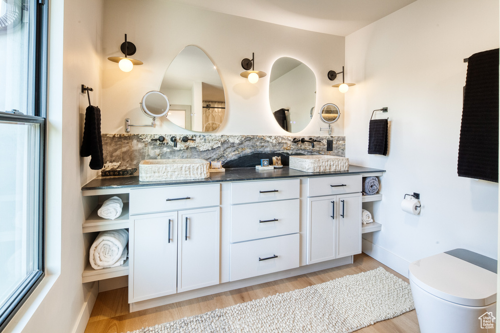 Full bathroom with double vanity, tasteful backsplash, wood finished floors, baseboards, and toilet