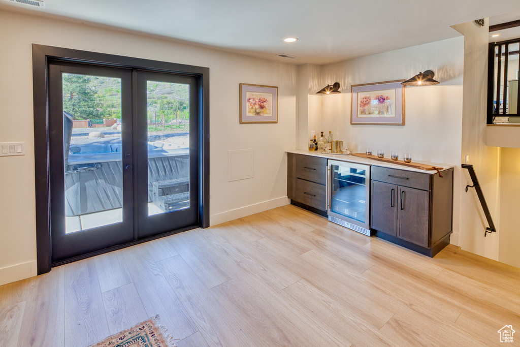 Bar featuring a bar, beverage cooler, baseboards, light wood-type flooring, and french doors