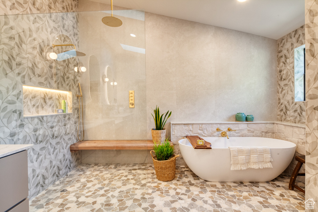 Full bath featuring a walk in shower, a freestanding tub, stone finish floor, and vanity