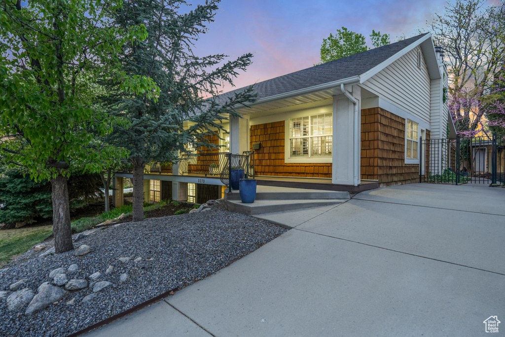 Property exterior at dusk with fence, covered porch, and a shingled roof