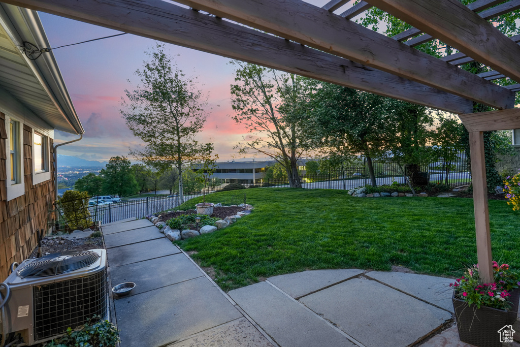 Yard at dusk with central air condition unit, a pergola, fence, and a patio area