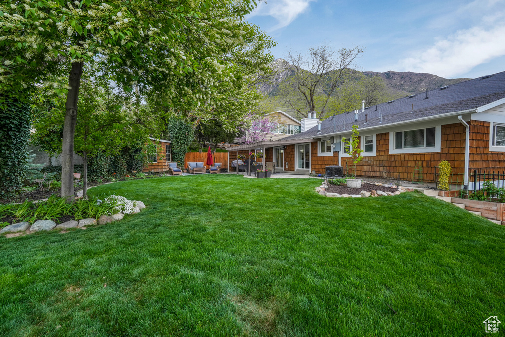 Rear view of property with a shingled roof, central AC, a mountain view, a patio area, and a lawn
