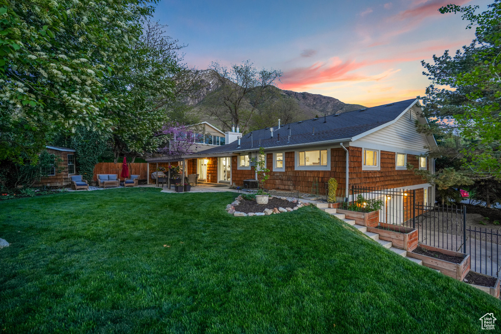 Back of house at dusk with fence, a patio, an outdoor hangout area, and a lawn