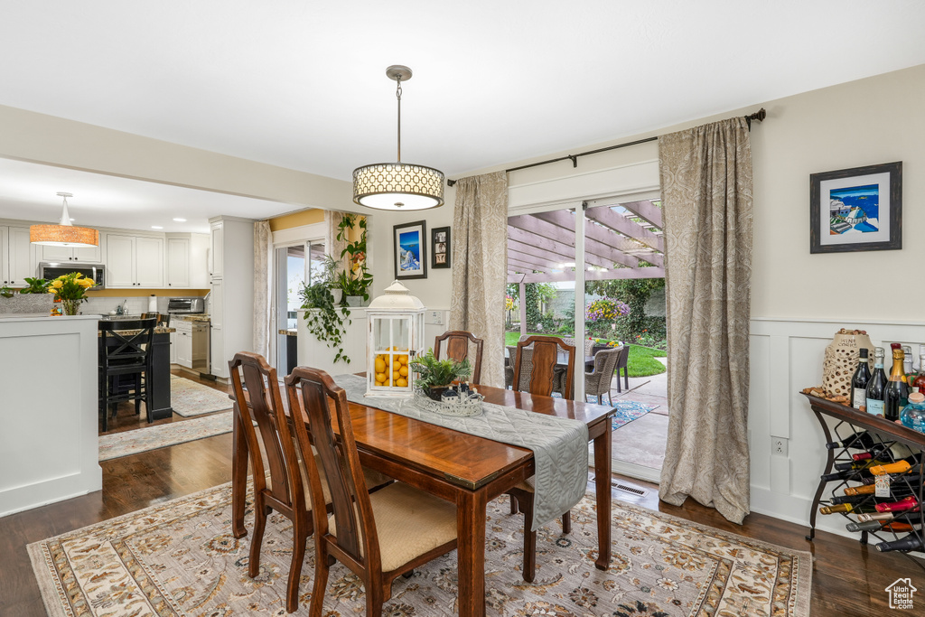 Dining space featuring wainscoting, dark wood-style flooring, and a decorative wall
