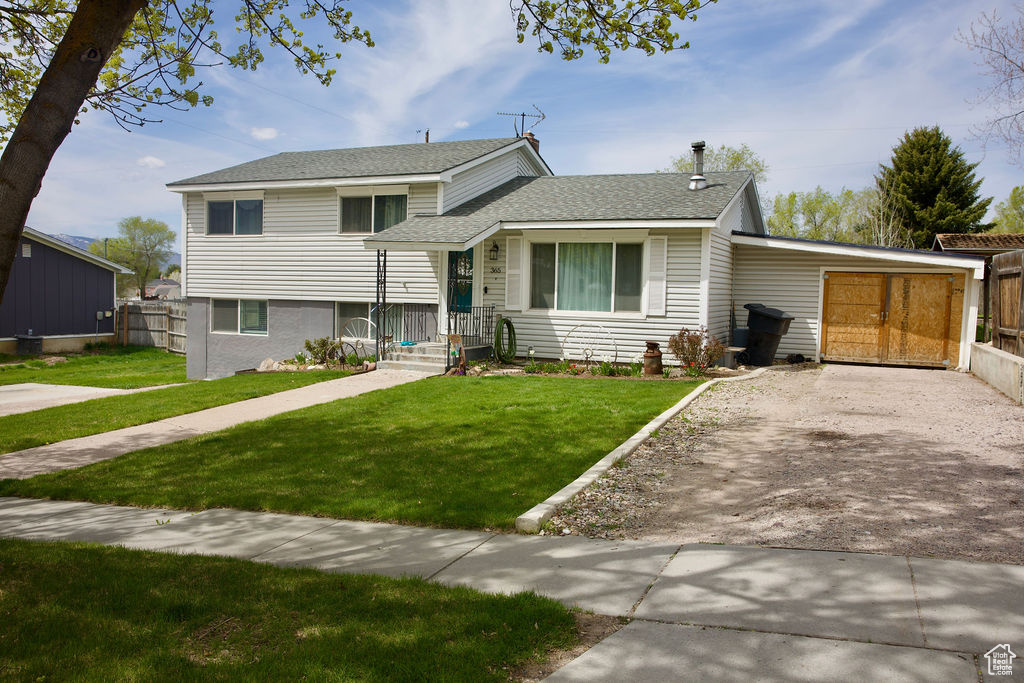 Split level home with fence, roof with shingles, driveway, and a front lawn