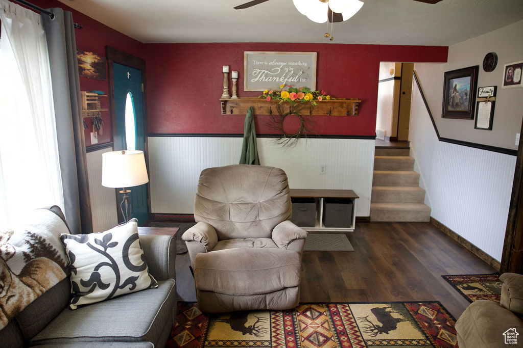Living area with stairs, wood finished floors, baseboards, ceiling fan, and a wainscoted wall