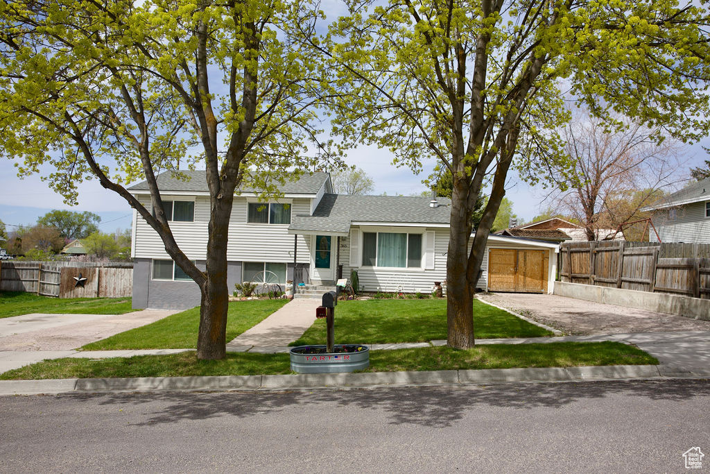 Split level home with fence, roof with shingles, and a front lawn