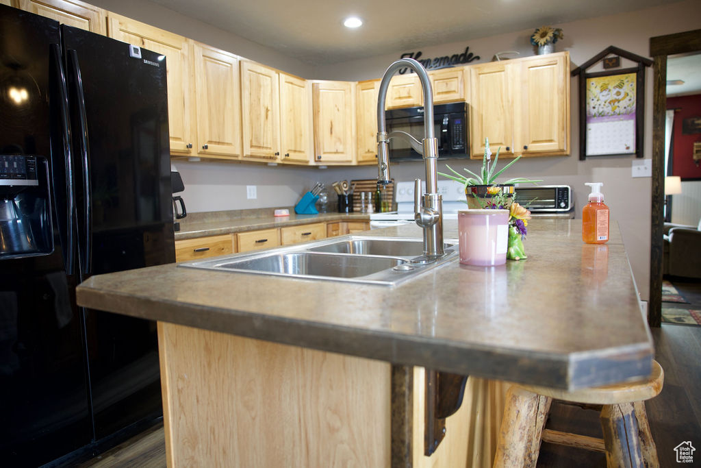 Kitchen featuring a breakfast bar, a sink, light brown cabinets, recessed lighting, and black appliances