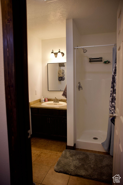 Full bathroom featuring vanity, tile patterned flooring, a shower stall, and a textured ceiling