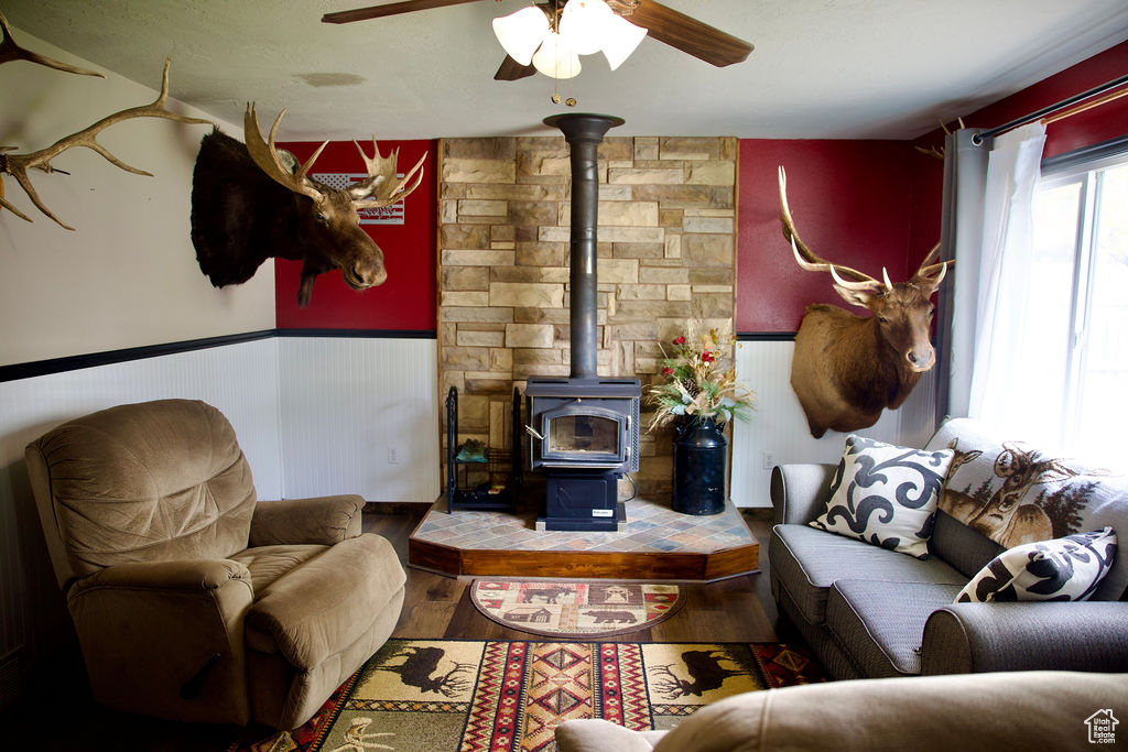 Living area featuring a ceiling fan, wainscoting, wood finished floors, and a wood stove