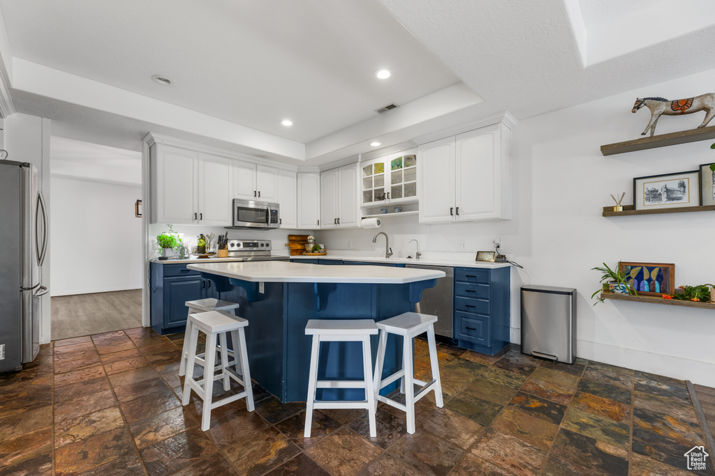 Kitchen featuring blue cabinets, a kitchen bar, appliances with stainless steel finishes, stone tile flooring, and a tray ceiling