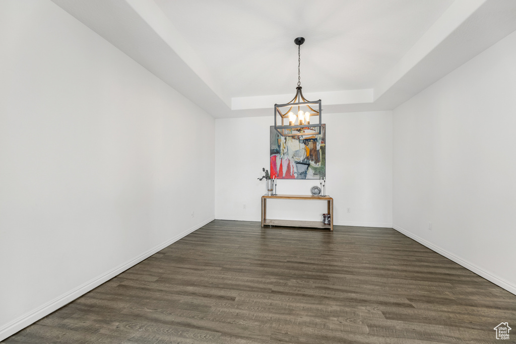 Empty room with dark wood-style flooring, baseboards, an inviting chandelier, and a raised ceiling