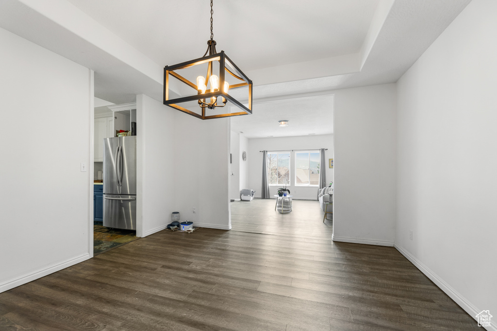 Unfurnished dining area with an inviting chandelier, baseboards, and dark wood-style floors