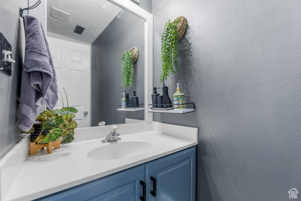 Bathroom with a textured wall, visible vents, and vanity