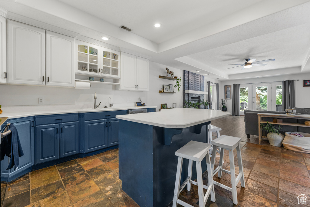 Kitchen with a breakfast bar area, blue cabinets, a sink, a tray ceiling, and stone tile floors