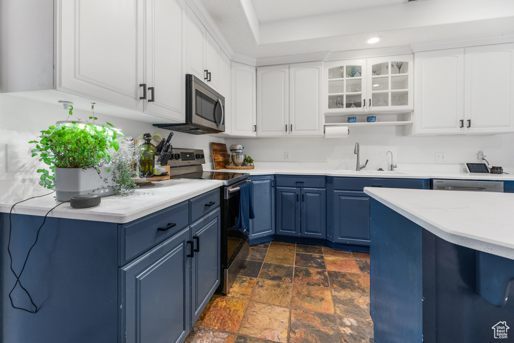 Kitchen with stone tile floors, light countertops, a sink, appliances with stainless steel finishes, and blue cabinetry