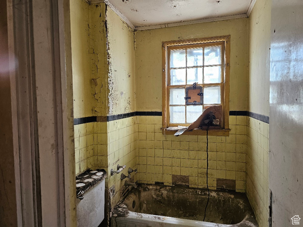 Full bath with tile walls, ornamental molding, a tub to relax in, and a wainscoted wall