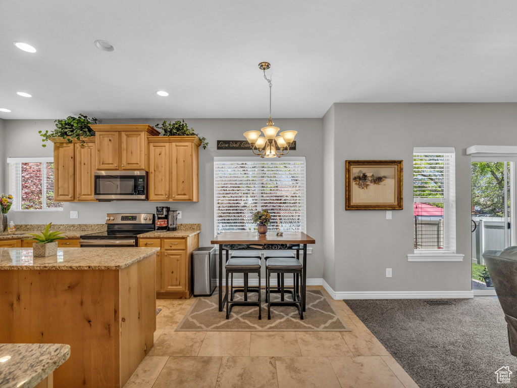 Kitchen featuring a notable chandelier, appliances with stainless steel finishes, light stone counters, recessed lighting, and decorative light fixtures