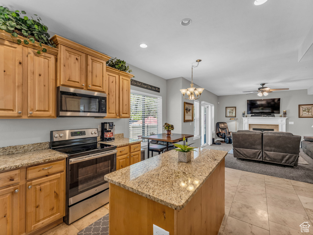 Kitchen with a kitchen island, appliances with stainless steel finishes, light stone counters, ceiling fan with notable chandelier, and open floor plan