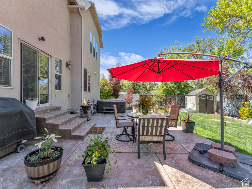 View of patio with a hot tub, an outdoor structure, a fenced backyard, a storage unit, and entry steps