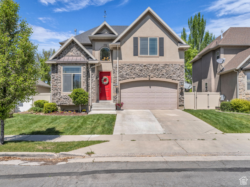 Craftsman-style house featuring a garage, fence, stucco siding, and stone siding