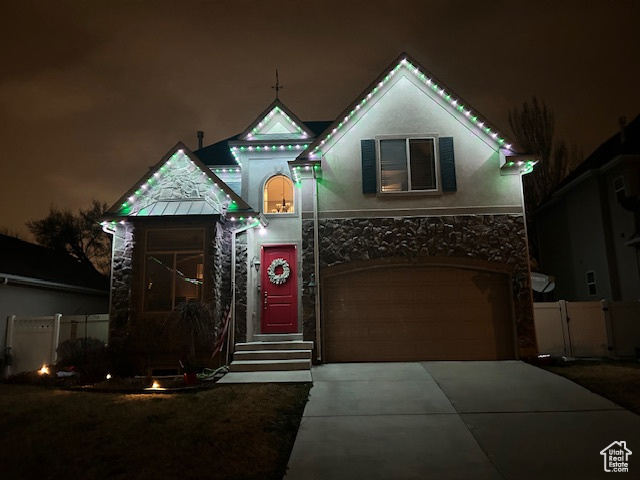 View of front of home with driveway, a garage, fence, stone siding, and stucco siding