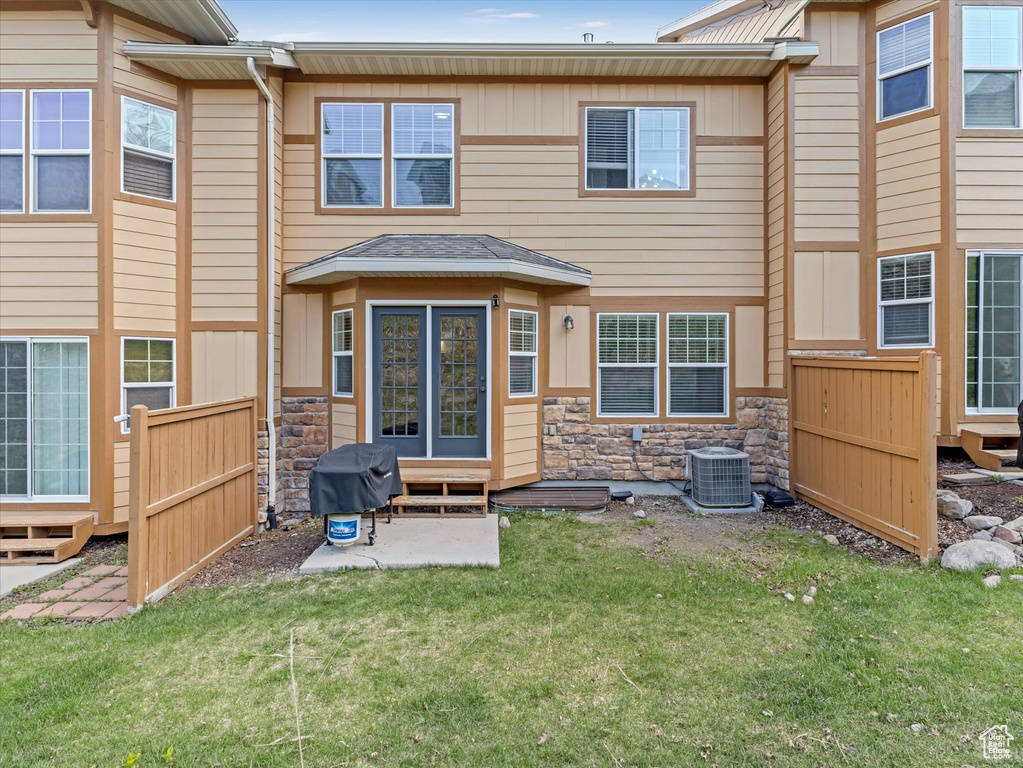 Rear view of house with fence, stone siding, cooling unit, entry steps, and a yard