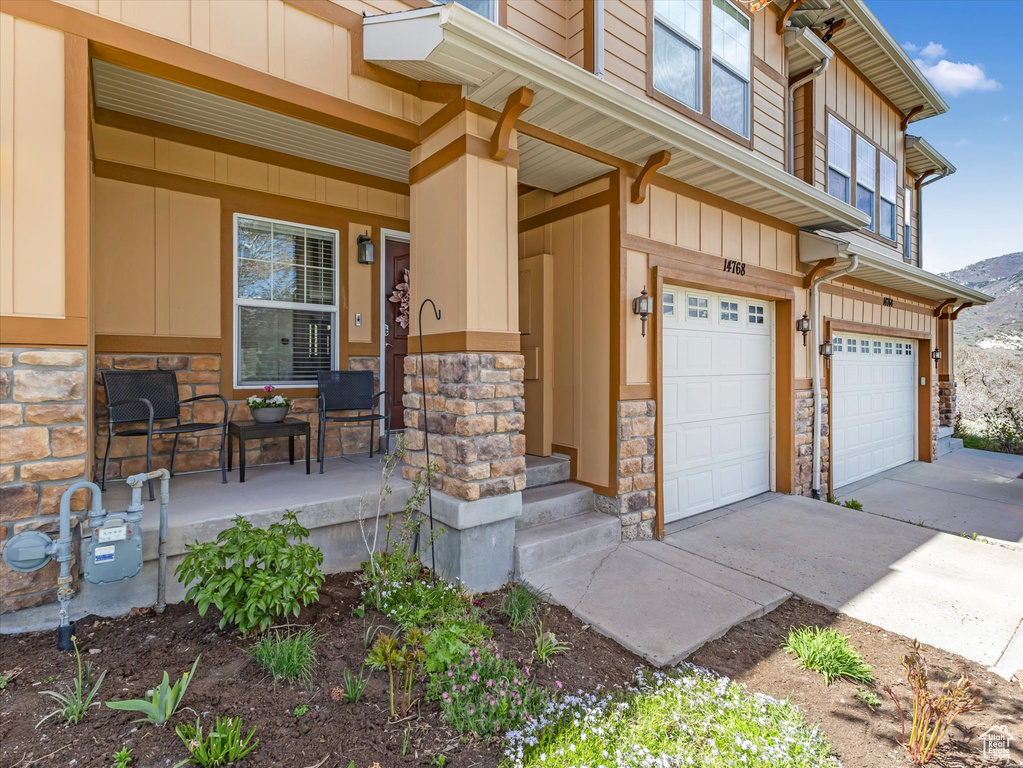 Doorway to property with an attached garage, stone siding, board and batten siding, concrete driveway, and a porch