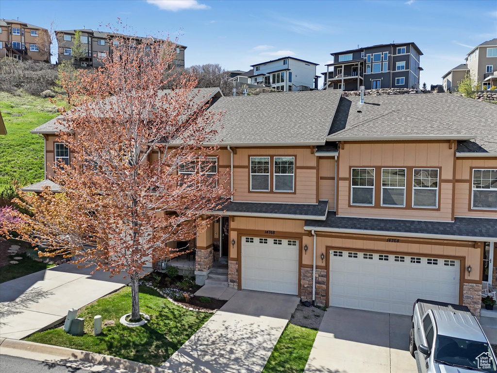 Townhome / multi-family property with concrete driveway, an attached garage, board and batten siding, and stone siding