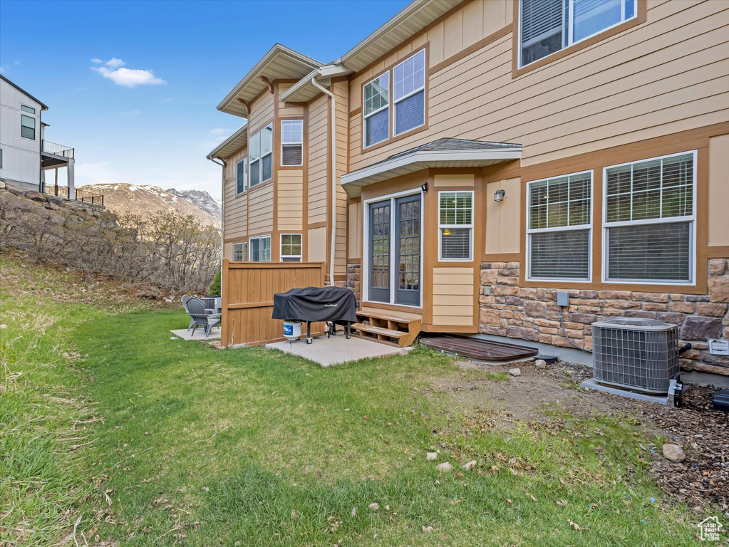 Back of property with entry steps, central AC unit, a mountain view, a lawn, and a patio