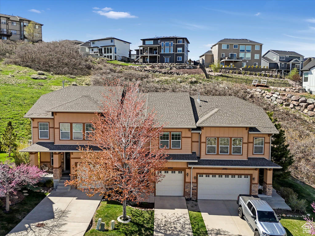 View of front of house featuring stone siding, roof with shingles, an attached garage, driveway, and a residential view