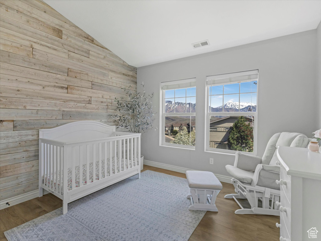 Bedroom with visible vents, lofted ceiling, wooden walls, and wood finished floors