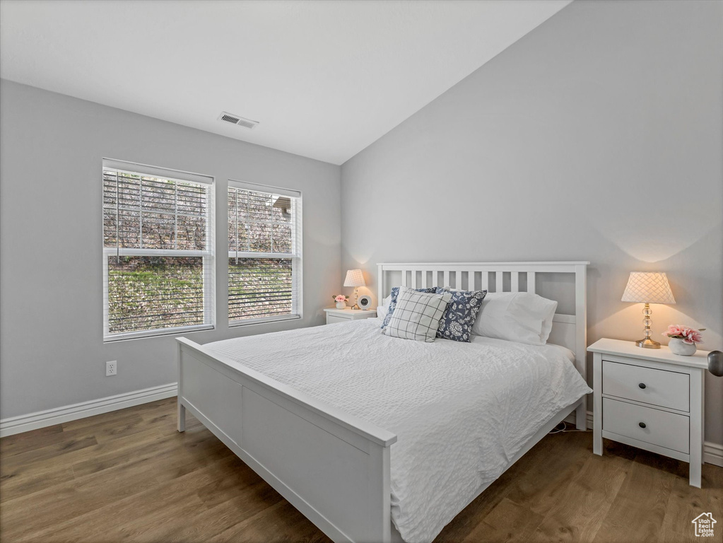 Bedroom with baseboards, vaulted ceiling, wood finished floors, and visible vents