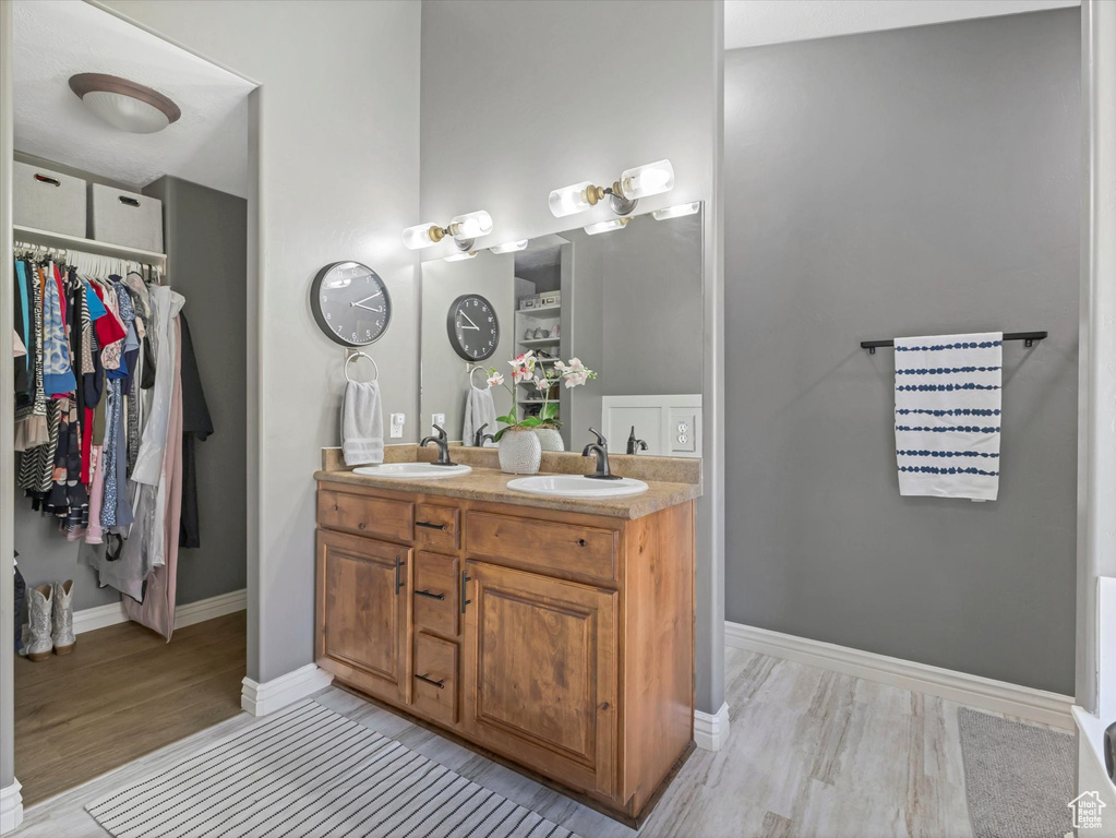 Full bath with a sink, a walk in closet, double vanity, and wood finished floors