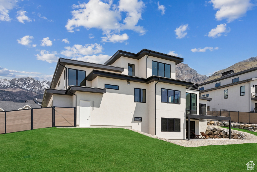Rear view of property with a garage, fence, stucco siding, a lawn, and a mountain view