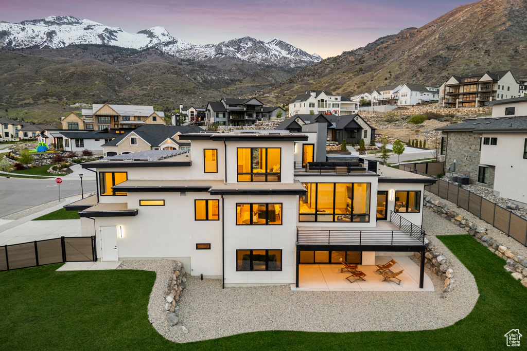 Back of property at dusk featuring a residential view, a fenced backyard, a patio area, a balcony, and a yard
